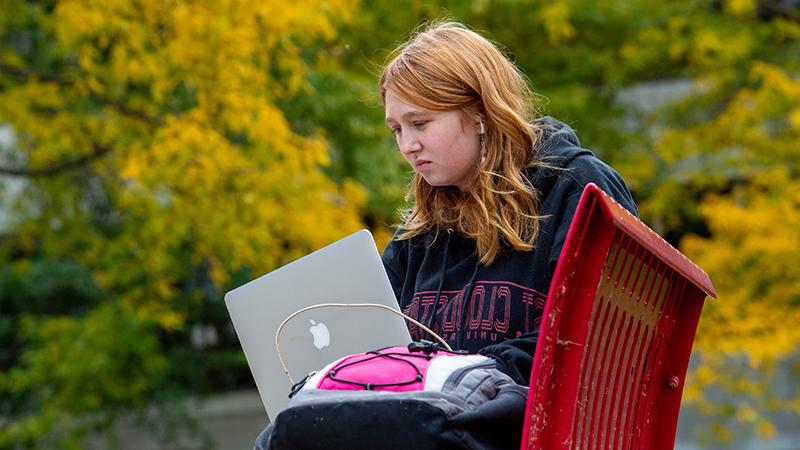 学生拿着笔记本电脑坐在长凳上